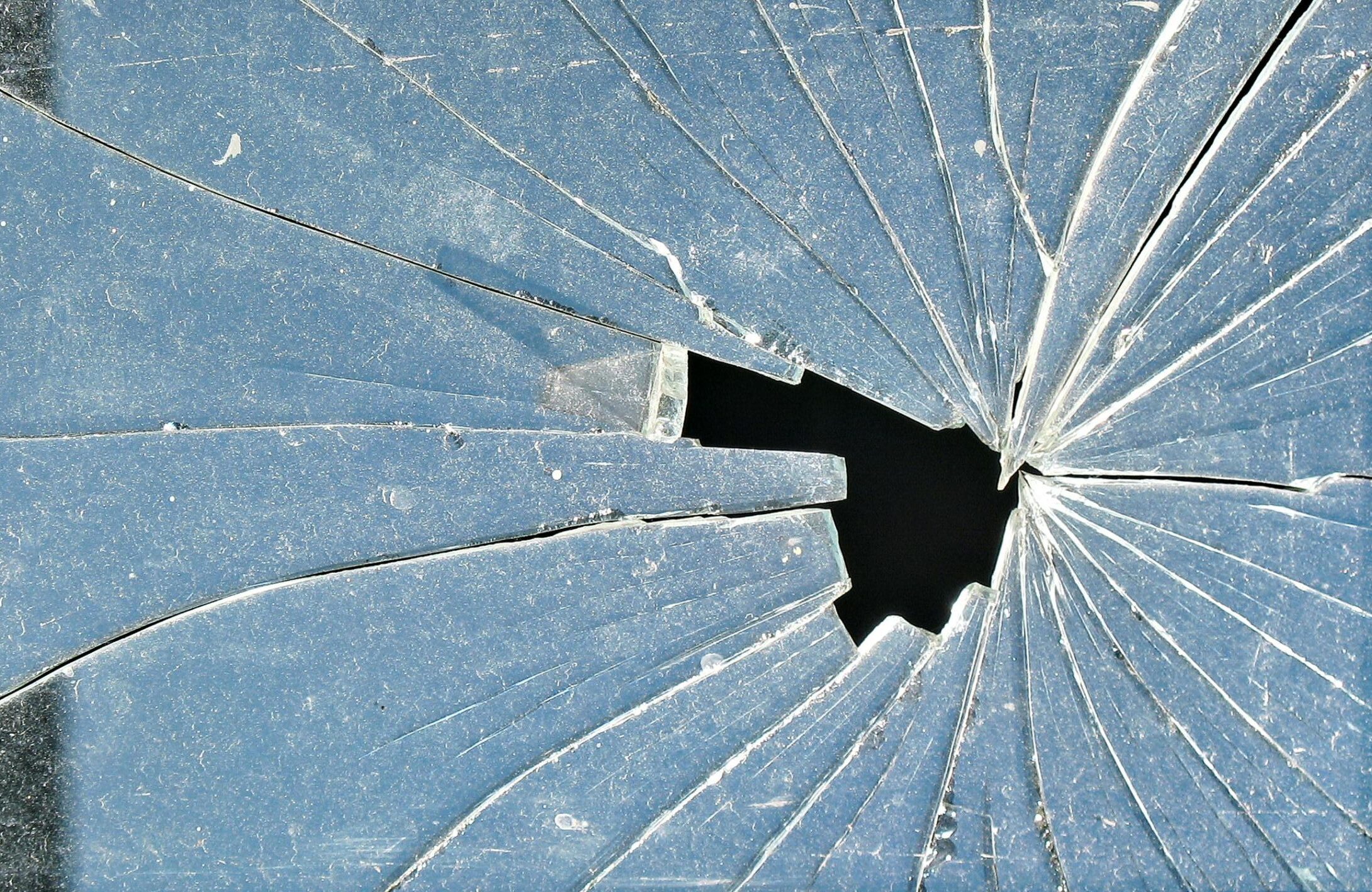 Close-up of cracked glass with a central hole, showcasing intricate patterns.