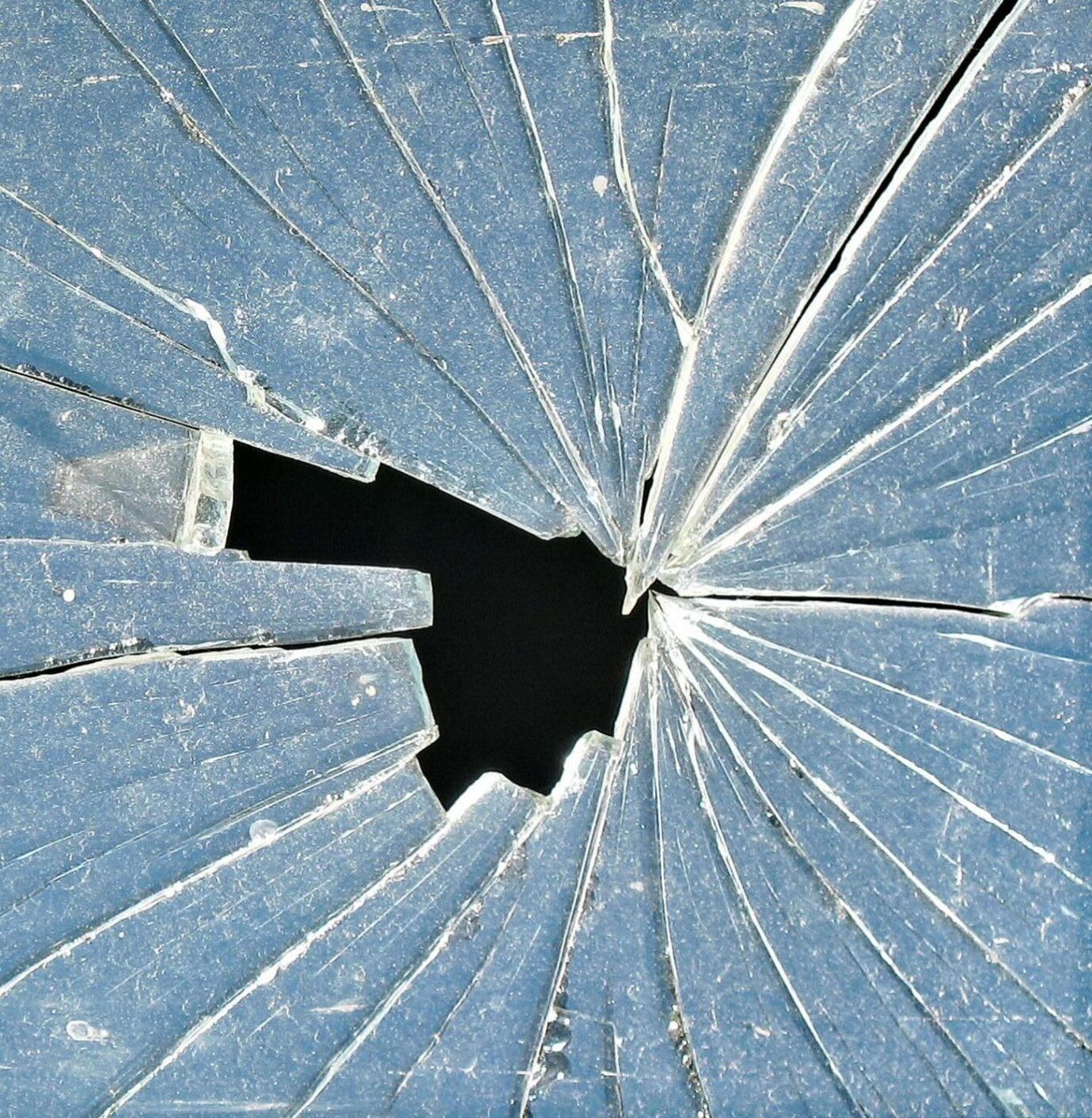Close-up of cracked glass with a central hole, showcasing intricate patterns.