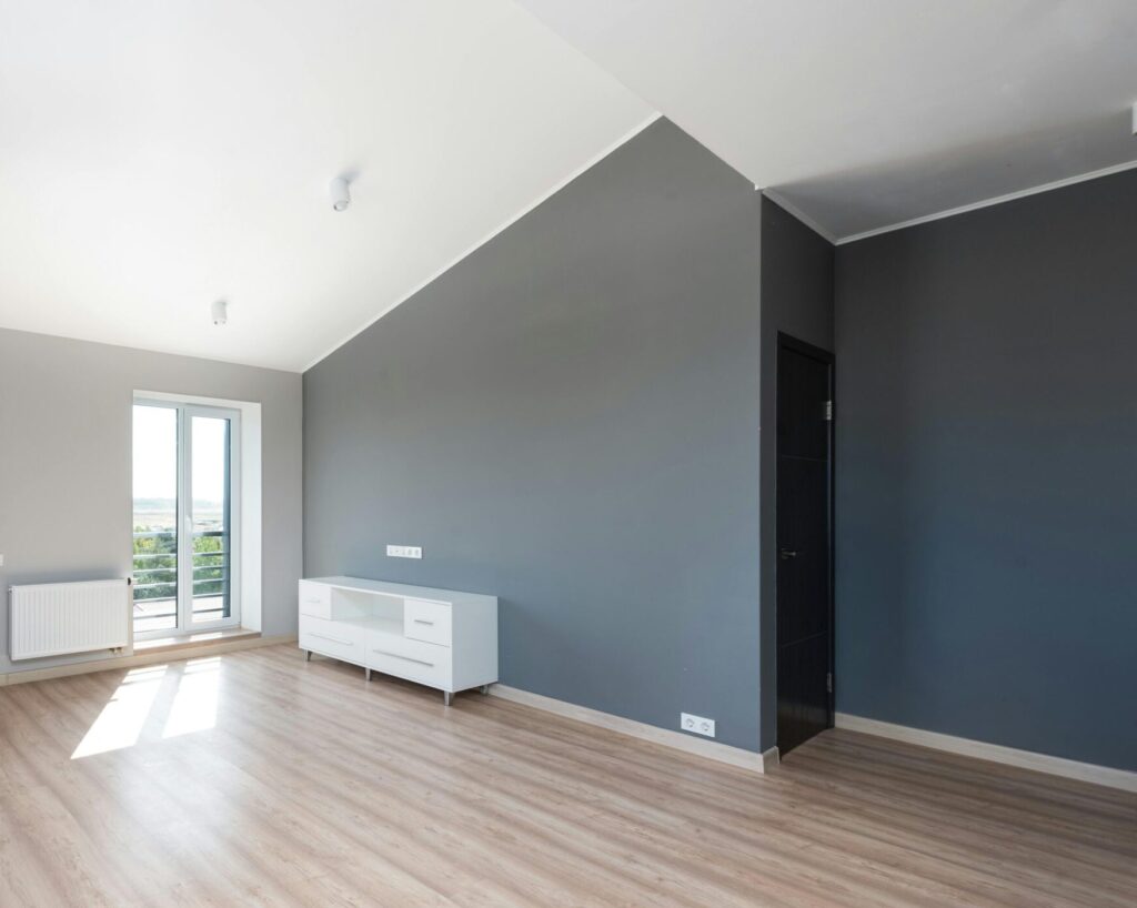 Wide-angle shot of a modern unfurnished apartment with wooden flooring and large windows.